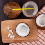 top-view-pulps-coconut-wooden-kitchen-board-with-knife-glass-water-checked-tablecloth-black-surface_141793-16086