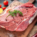 front-view-fresh-raw-red-meat-wooden-cutting-board-nude-color-towel-lemon-garlic-mixed-color-background